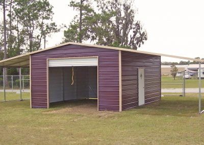 A purple metal garage with a white door is sitting in the middle of a grassy field.