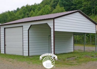 A white garage with a brown roof is sitting in the middle of a grassy field.