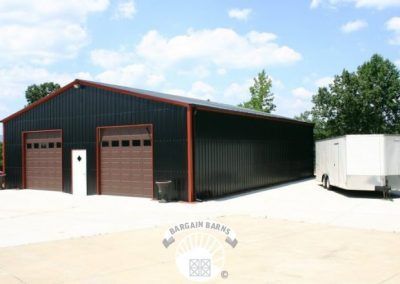 A large black metal building with two garage doors and a trailer parked in front of it.