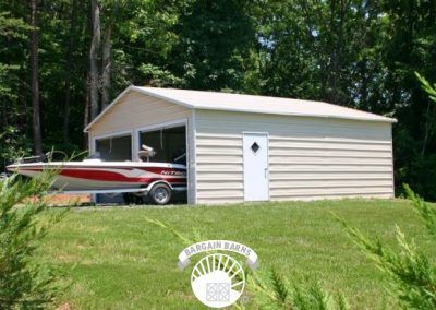 A boat is parked in a garage with trees in the background.