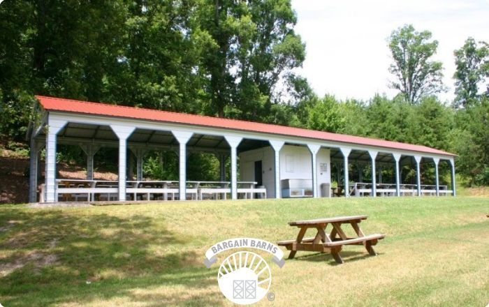 A long pavilion with a red roof and a picnic table in front of it