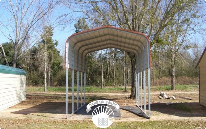 A carport is sitting in the middle of a field next to a tree.