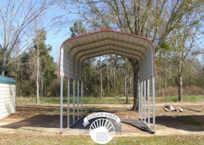 A metal carport is sitting in the middle of a field next to a tree.