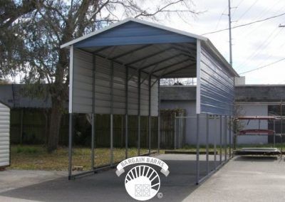 A metal carport with a blue roof is sitting in front of a building.