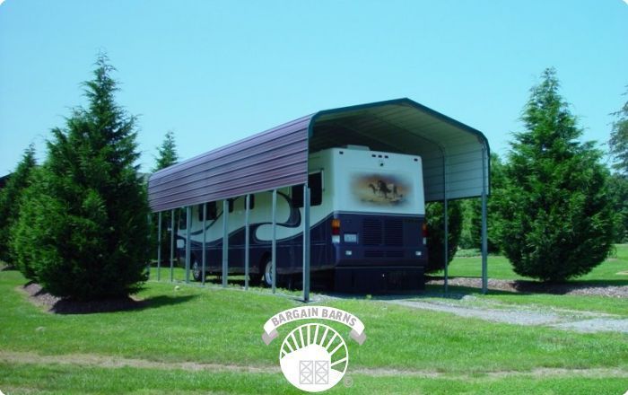 A rv is parked under a canopy in a grassy field