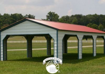 A white building with a red roof is in the middle of a grassy field.