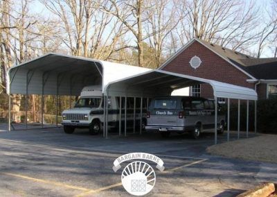 Two vans are parked under a carport in front of a brick building
