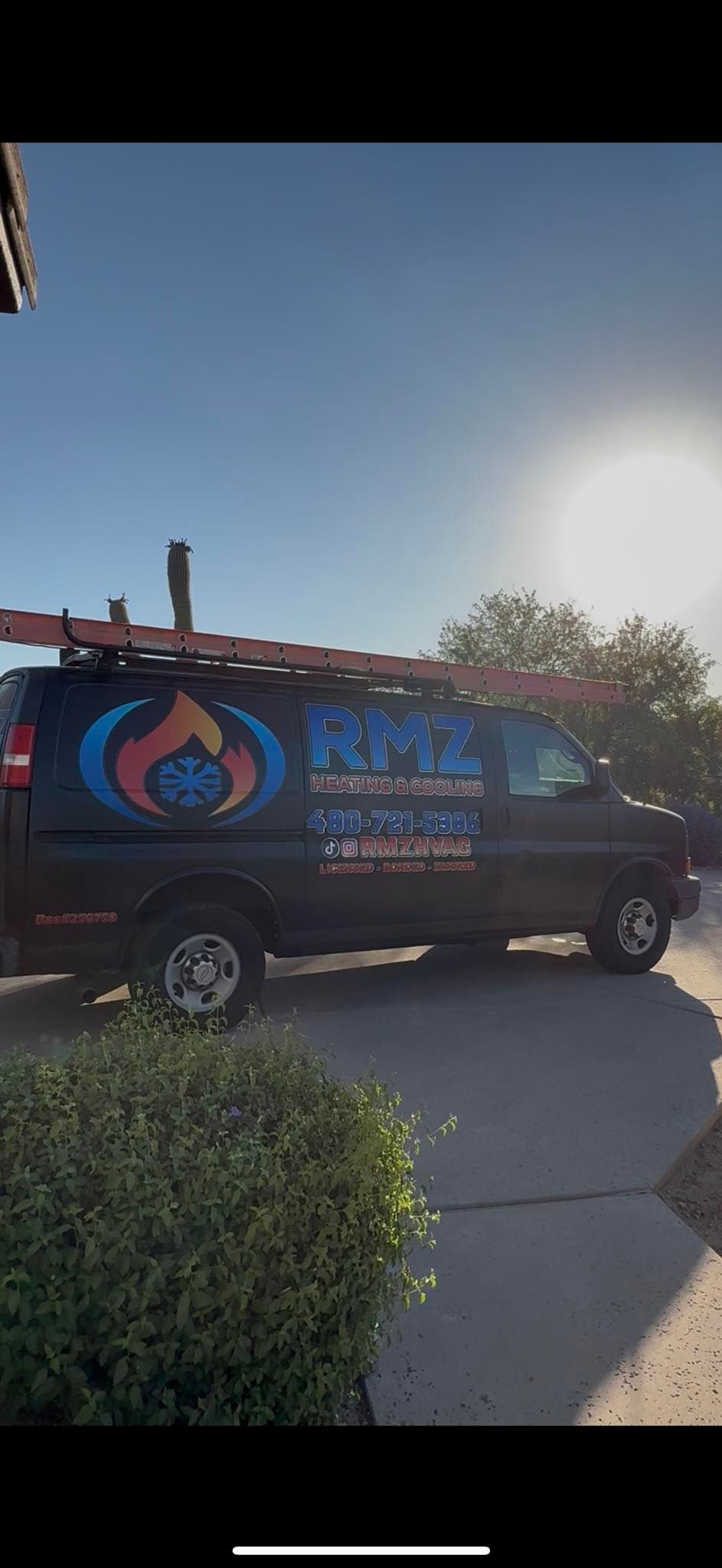A black van with a ladder on top of it is parked on the side of the road.