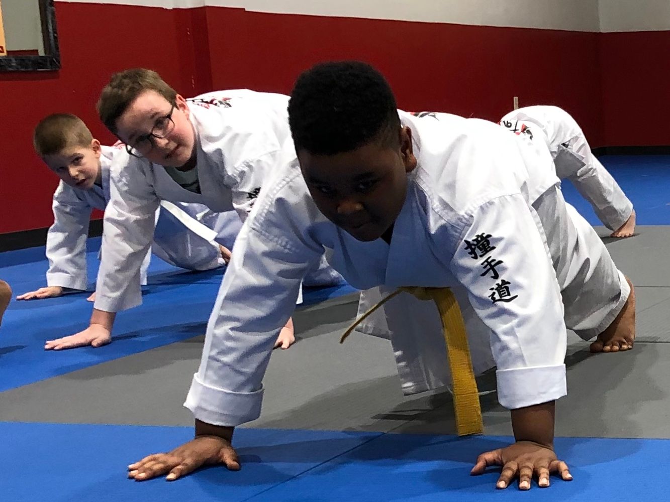 A group of young boys in karate uniforms are doing push ups on a blue mat.