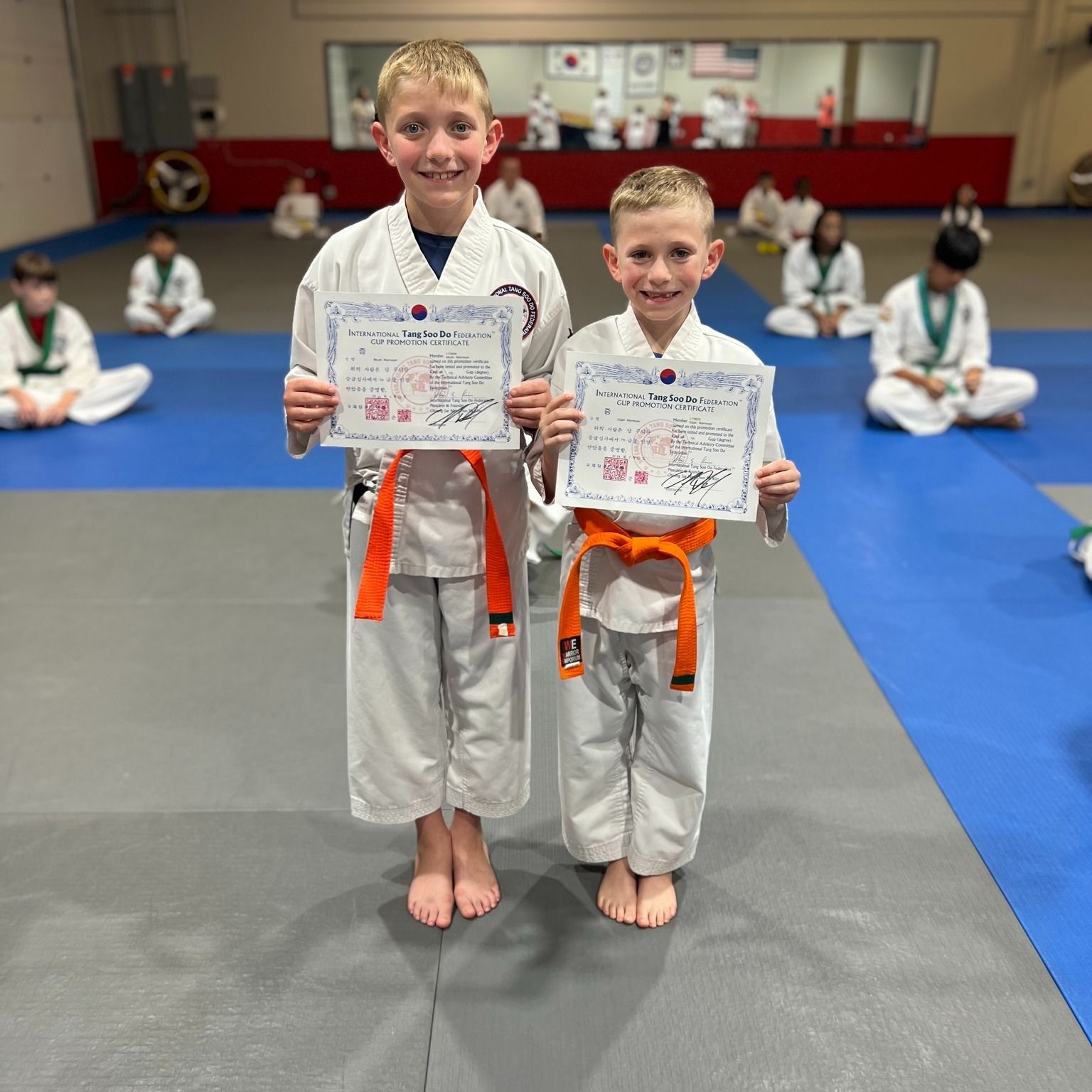 Two young boys in martial arts uniforms holding certificates