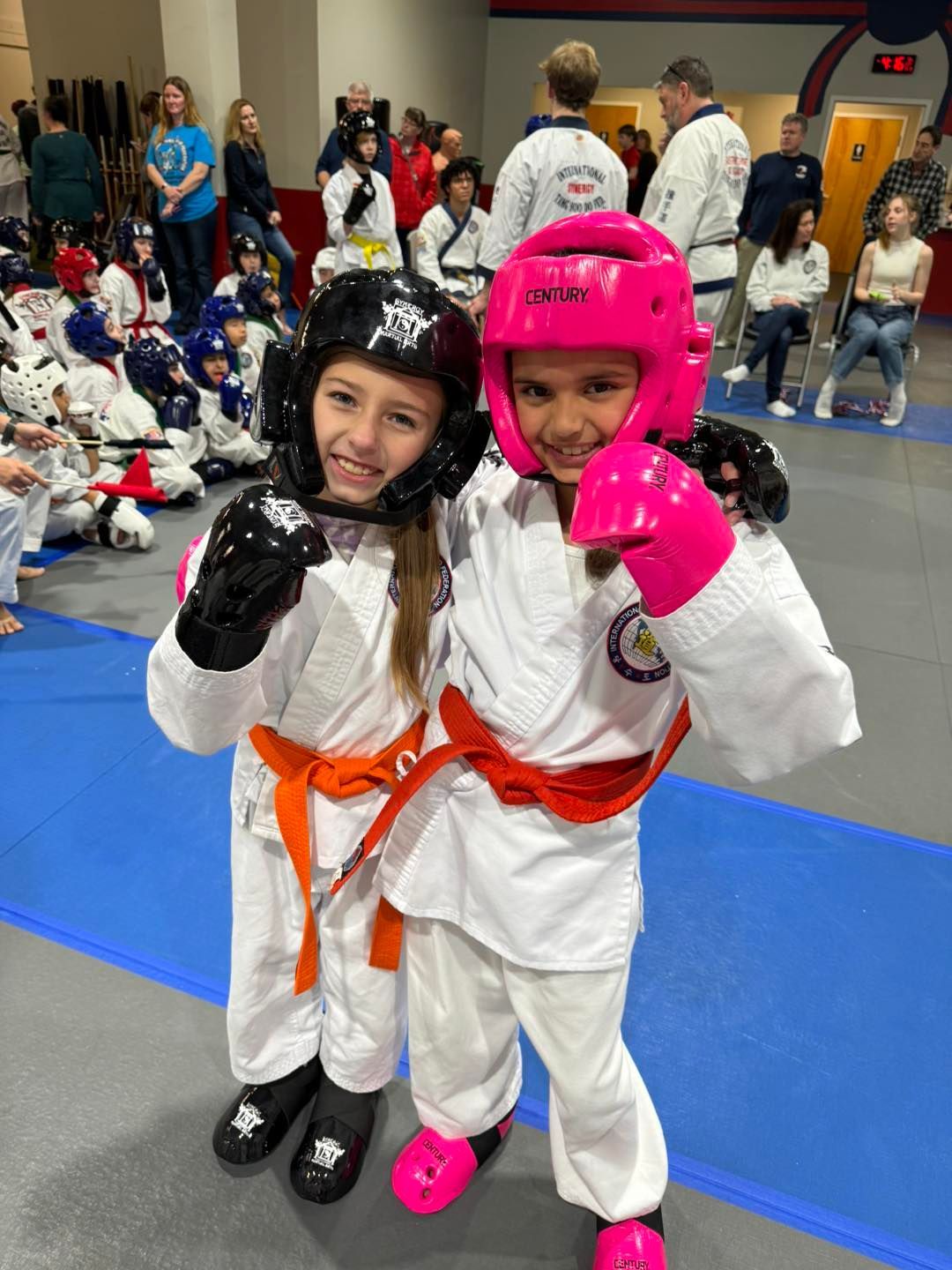 Two young girls wearing karate uniforms and pink gloves are posing for a picture.