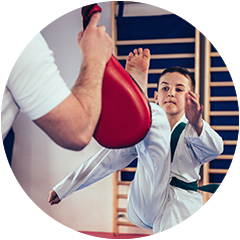 A young boy is practicing karate with a red kick pad.