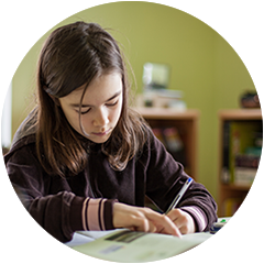 A young girl is writing on a piece of paper with a pen.