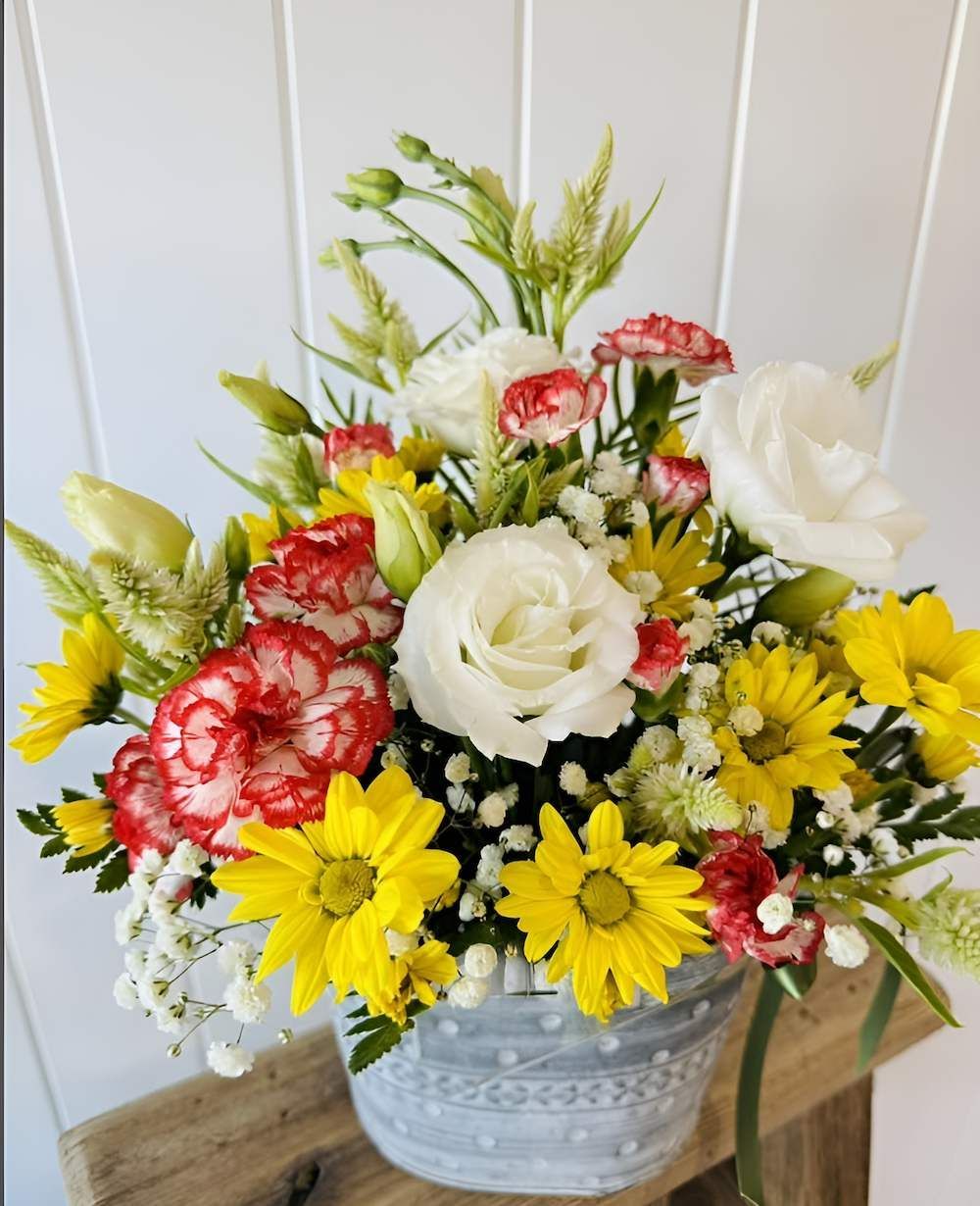A Vase Filled With Yellow and Red Flowers is Sitting on a Wooden Table — Bundaberg House of Flowers In Elliot Heads, QLD