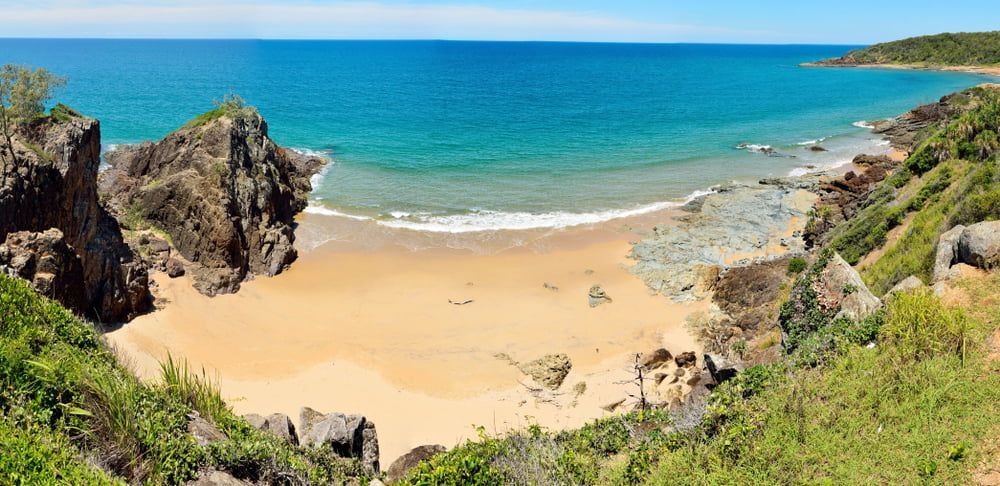 Secluded golden sand beach surrounded by rugged cliffs and lush greenery — Bundaberg House of Flowers In Coral Cove, QLD