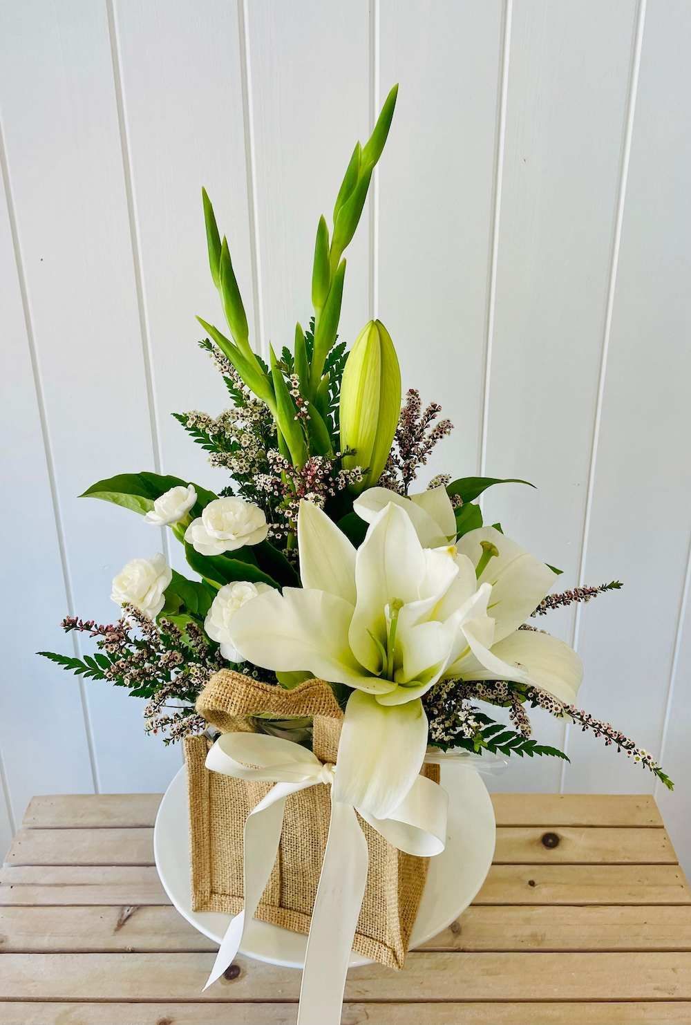 A Vase Filled With White Flowers is Sitting on a Wooden Table — Bundaberg House of Flowers In Burnett Heads, QLD