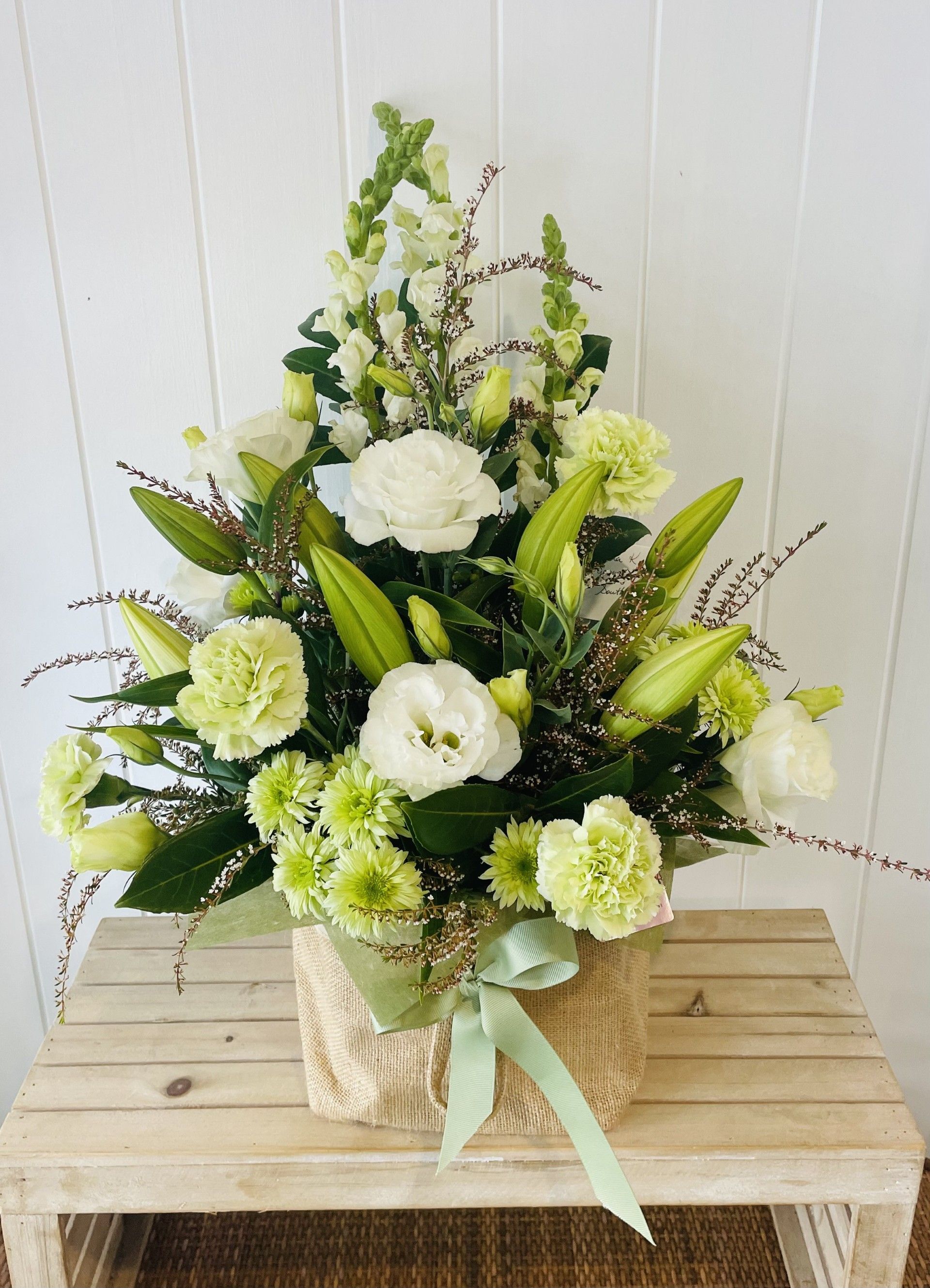 A Basket Filled With Green and White Flowers is Sitting on a Wooden Table — Bundaberg House of Flowers in Bundaberg West, QLD