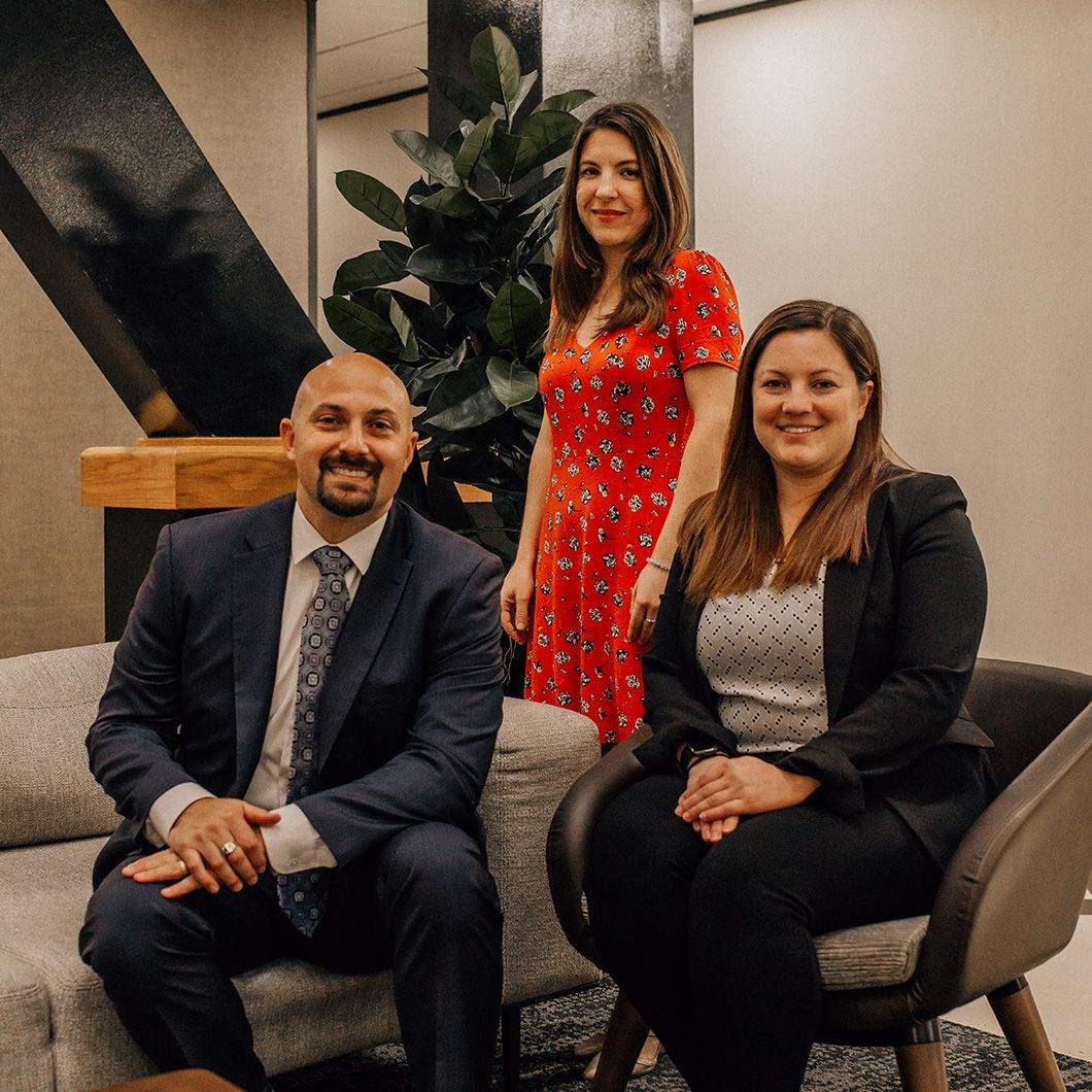 A man in a suit and tie is sitting on a couch next to two women.