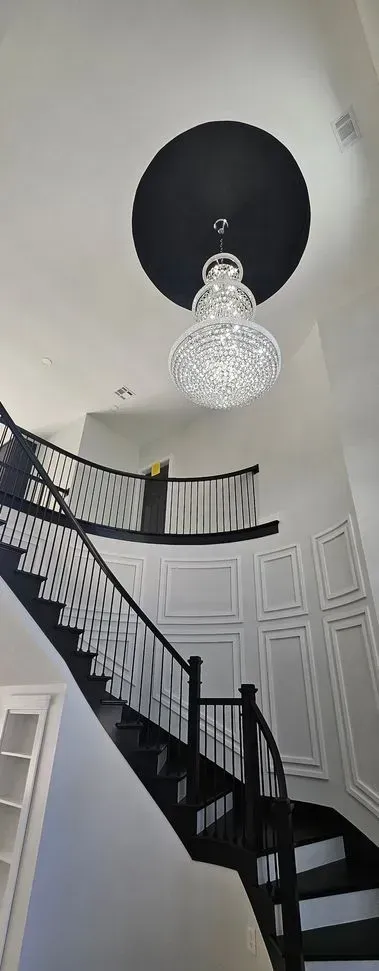 A black and white staircase with a chandelier hanging from the ceiling.