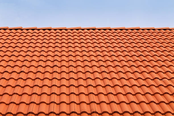 A close up of a red tiled roof with a blue sky in the background.