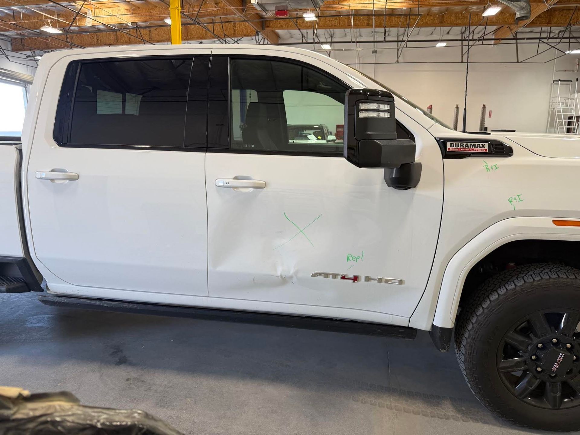 A man is looking under the fender of a car while holding a clipboard.