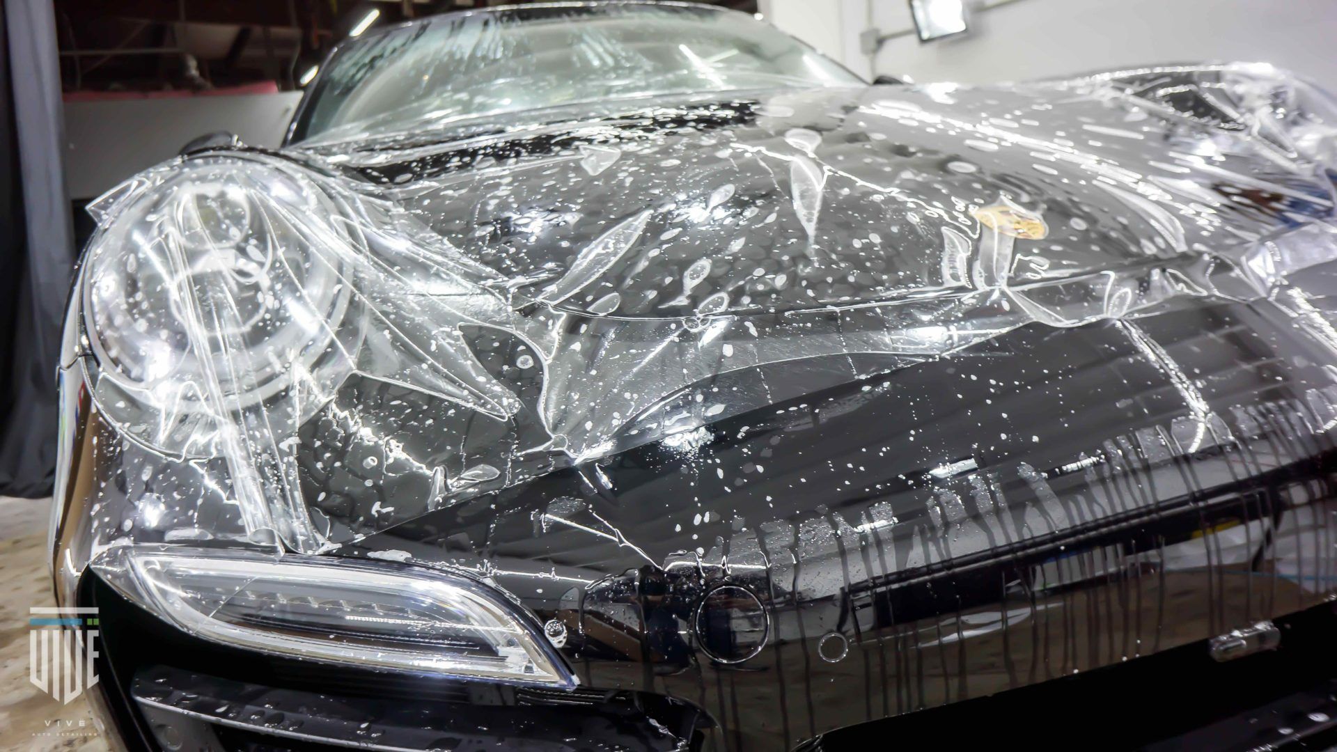 Black car with clear protective film being applied to the hood.