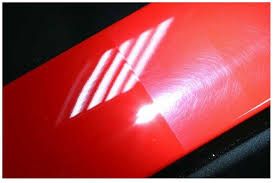 Red car panel with circular swirl marks reflecting striped light.