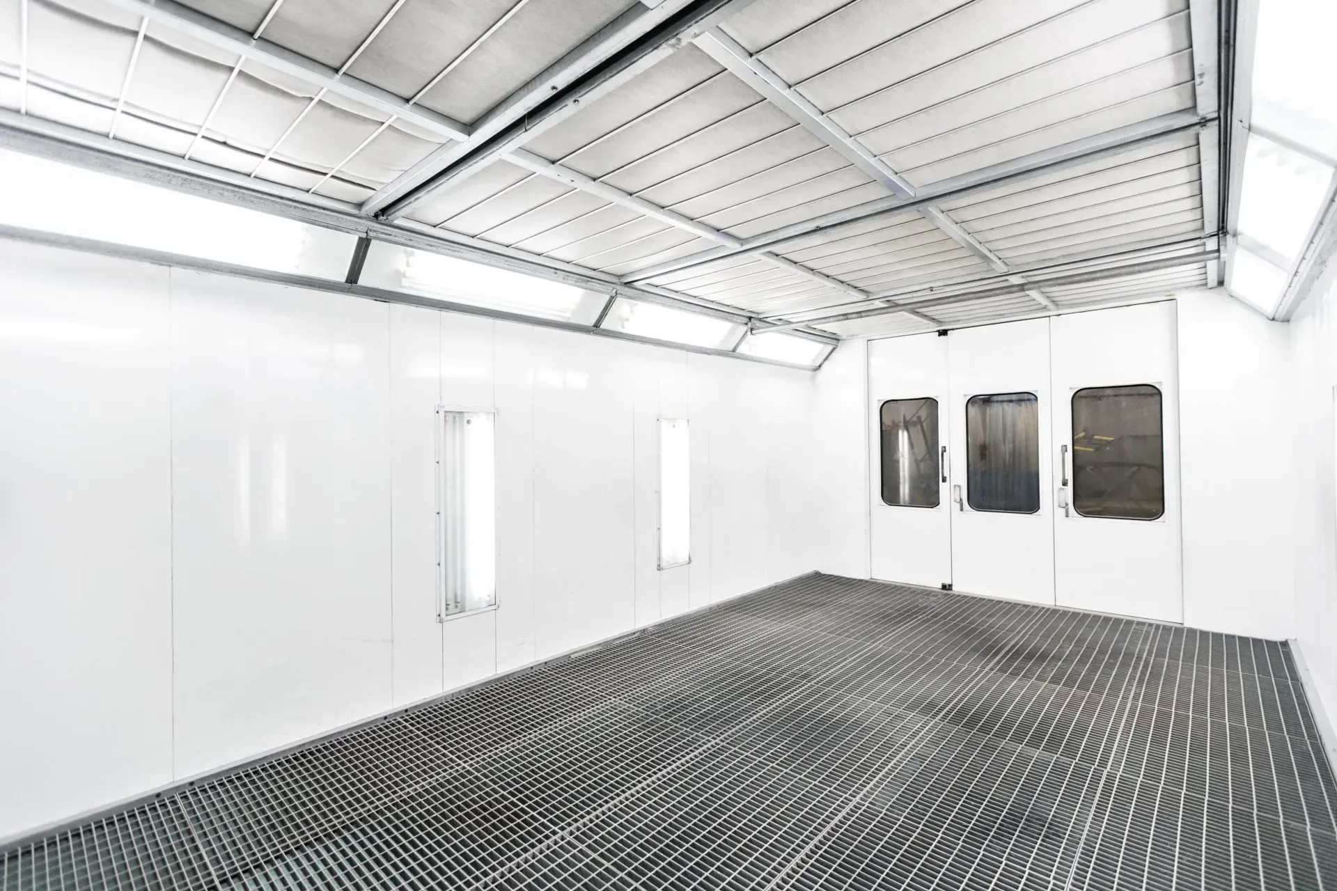White empty paint booth with grated floor, bright lighting.