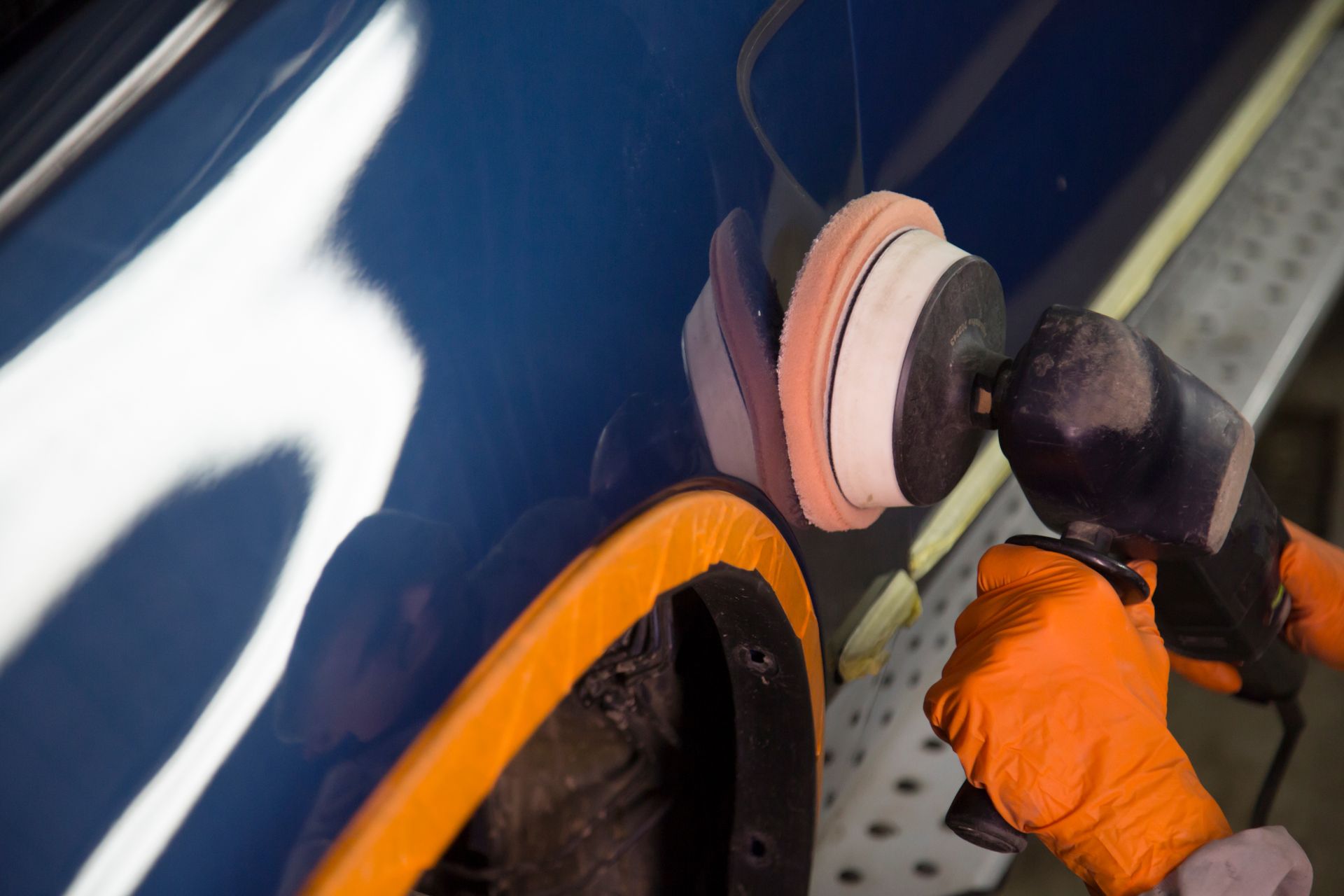 Auto body worker polishing a car door with an electric buffer.