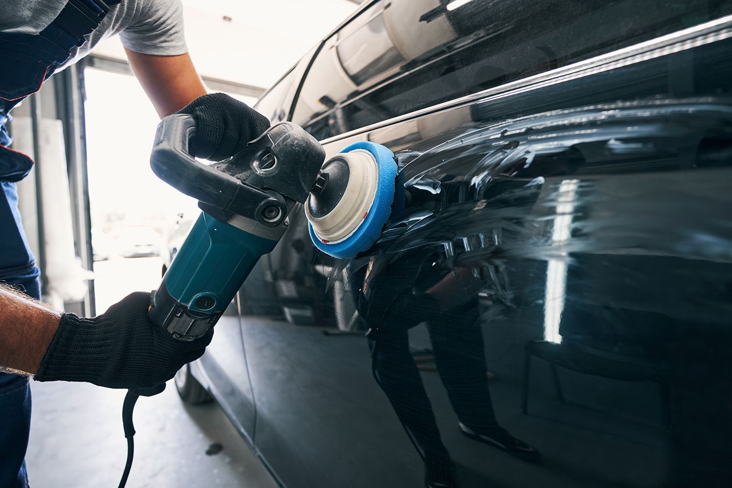 Automotive technician polishing a vehicle door with a power buffer to restore a smooth, glossy finis