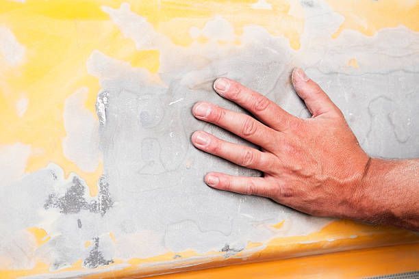Auto body repair worker sanding and smoothing filler on a car panel during vehicle restoration.