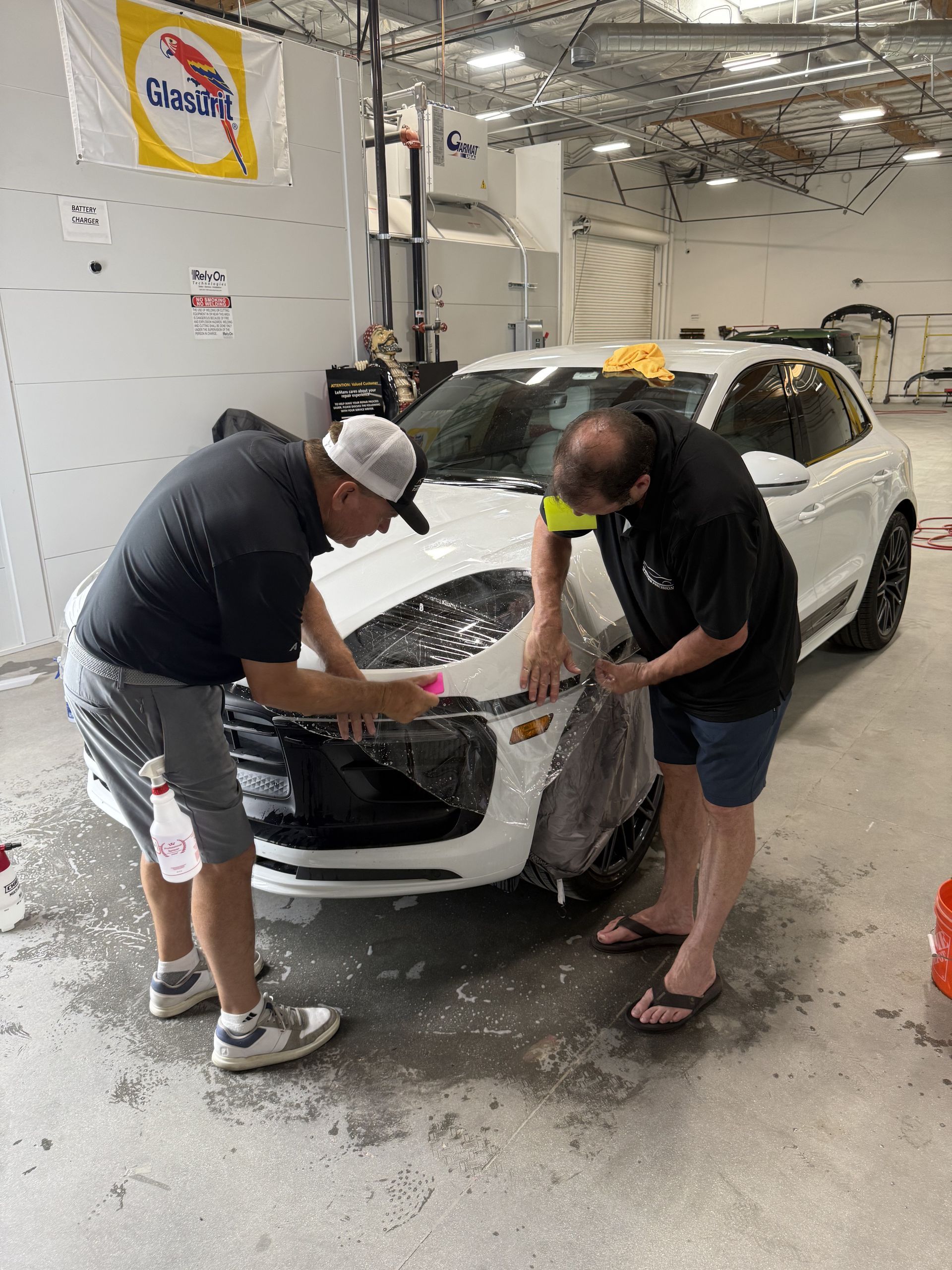 A man is looking under the fender of a car while holding a clipboard.