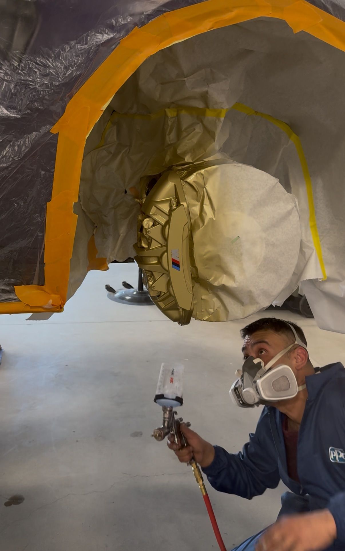 A man wearing a mask is spraying paint on a car fender.