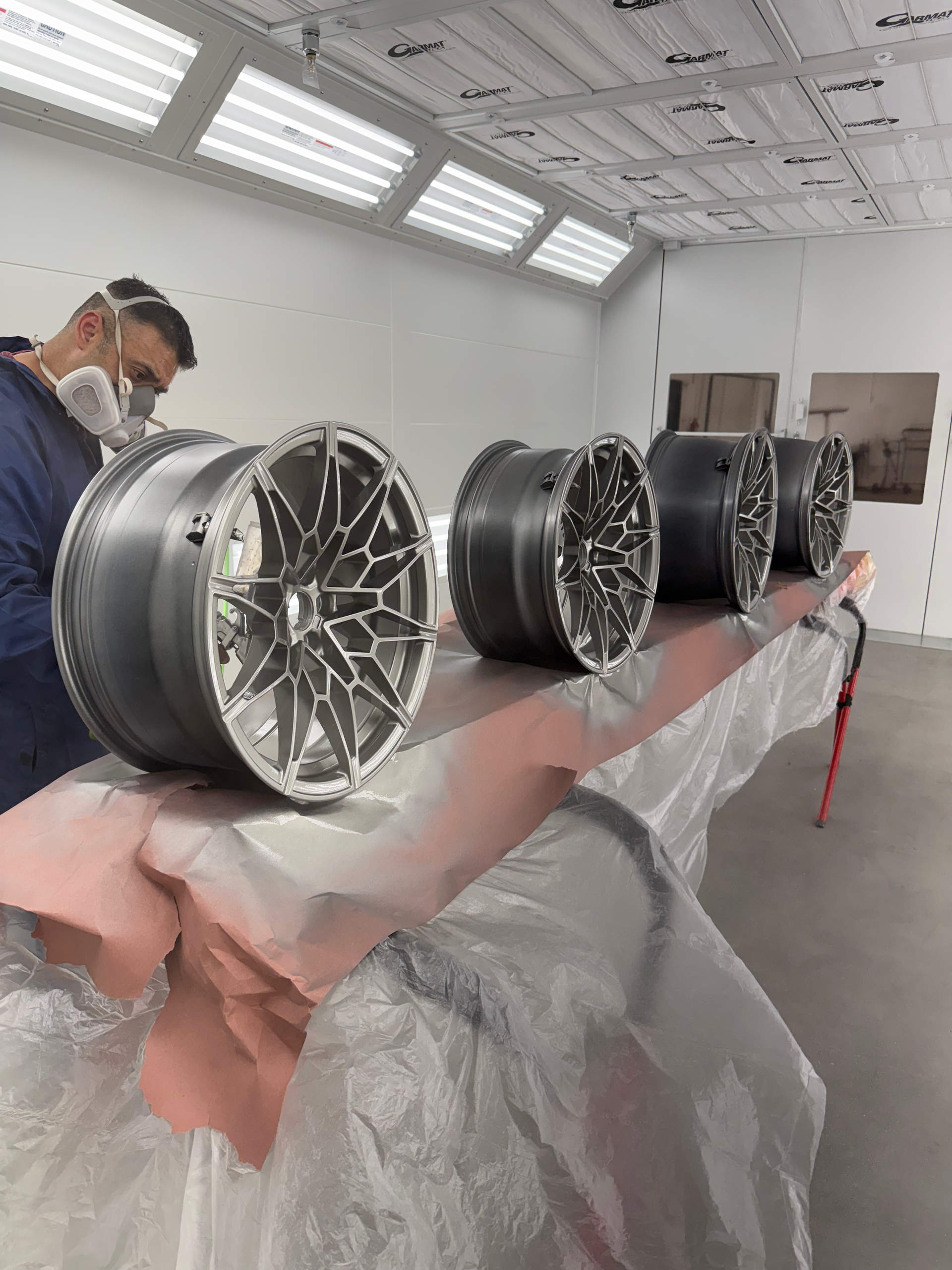 A man is painting a row of wheels in a paint booth.