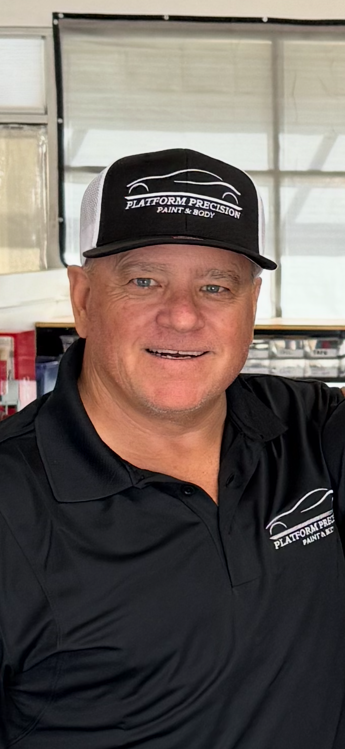 Man wearing a cap and polo shirt with a logo; smiling, in an indoor setting.