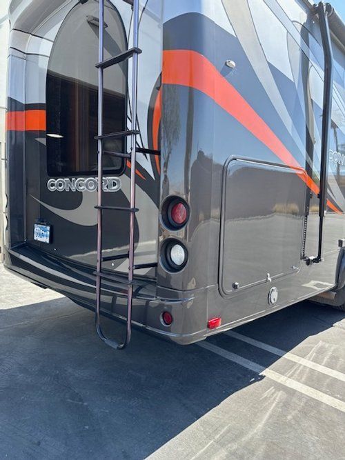 Rear view of a Concord RV in gray, orange, and black with ladder, storage, and taillights.