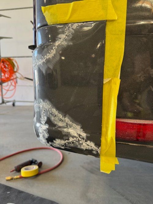 Black car bumper with body filler, taped for repair.