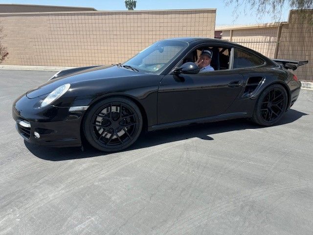 A black porsche 911 turbo is parked in a parking lot.
