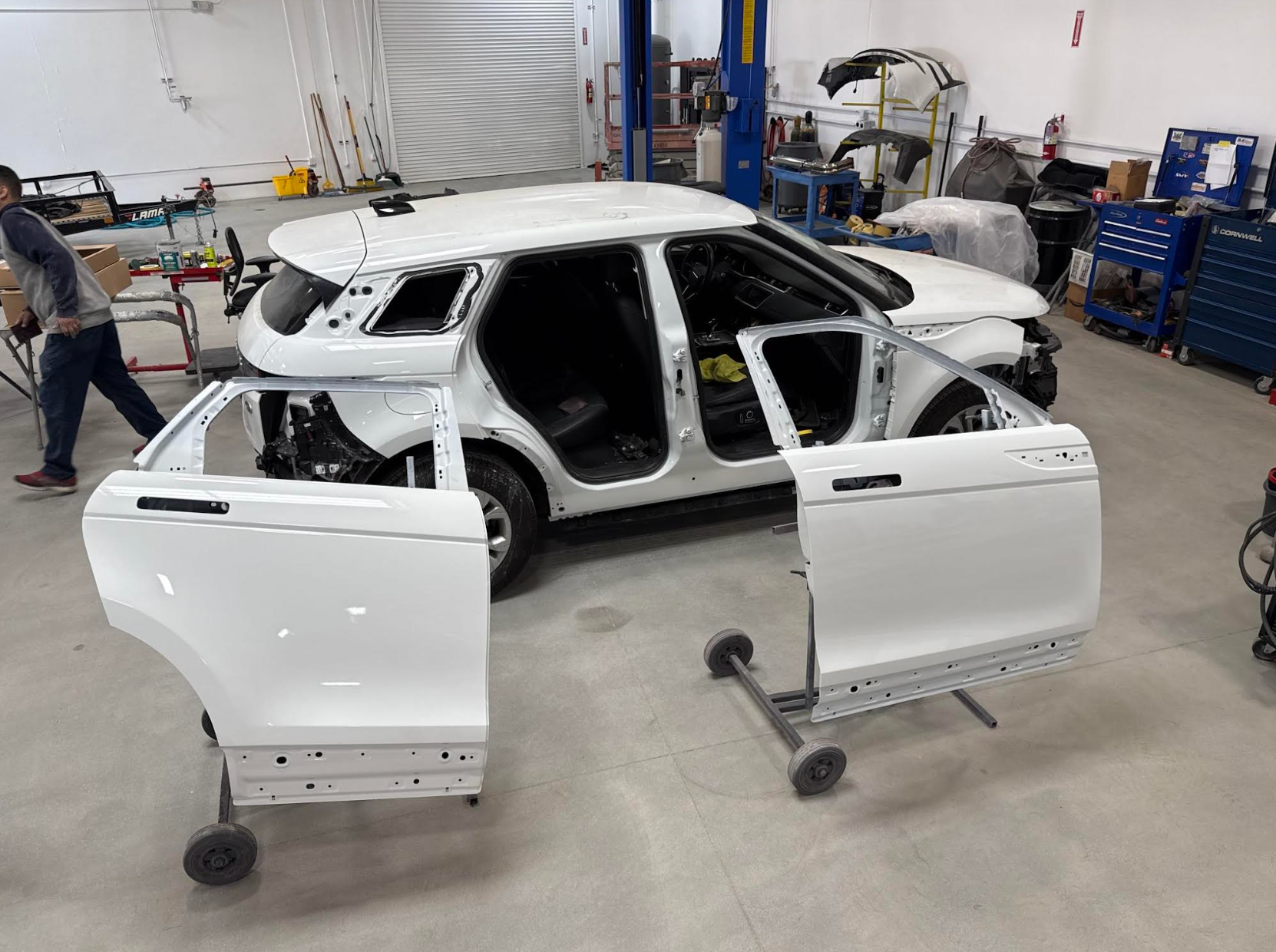 A white car is being built in a garage with the doors open.