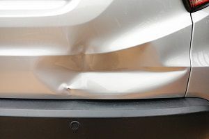 Auto technician aligning and adjusting a car’s rear bumper panel during vehicle body repair.