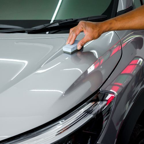 Hand applying ceramic coating to a car's gray hood, showcasing a glossy finish.