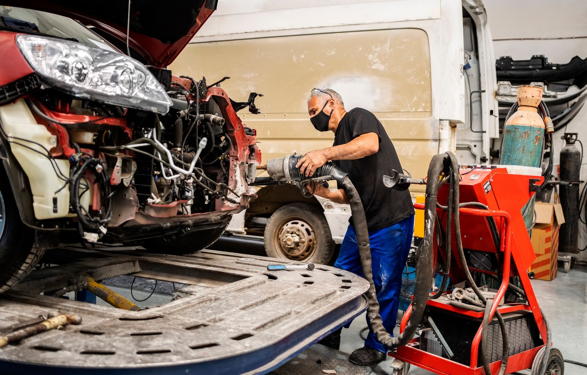 A mechanic at a car collision repair shop works on a vehicle using tools and equipment.