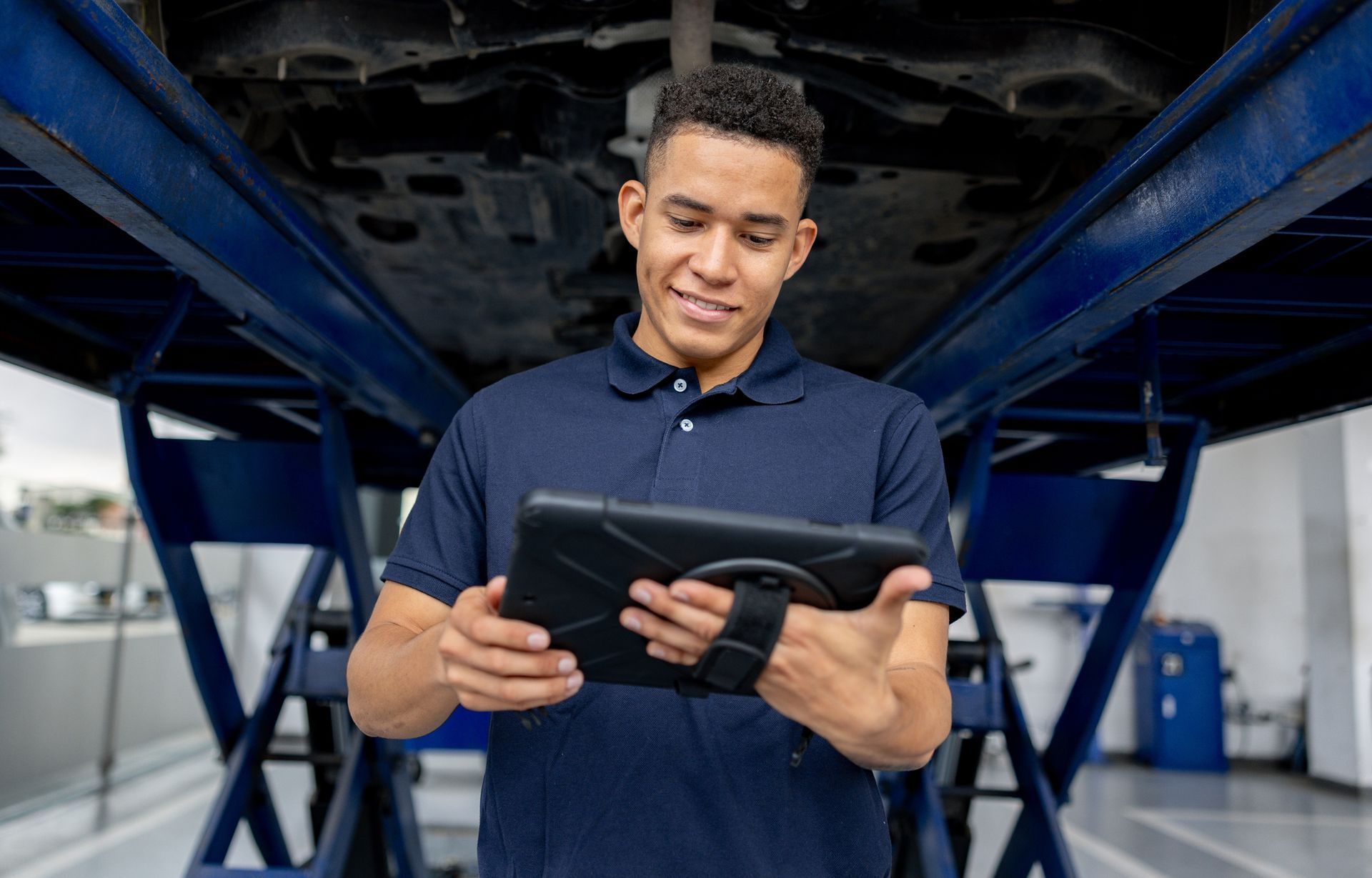 An auto technician using a digital tablet to inspect a vehicle lifted on a hydraulic car lift