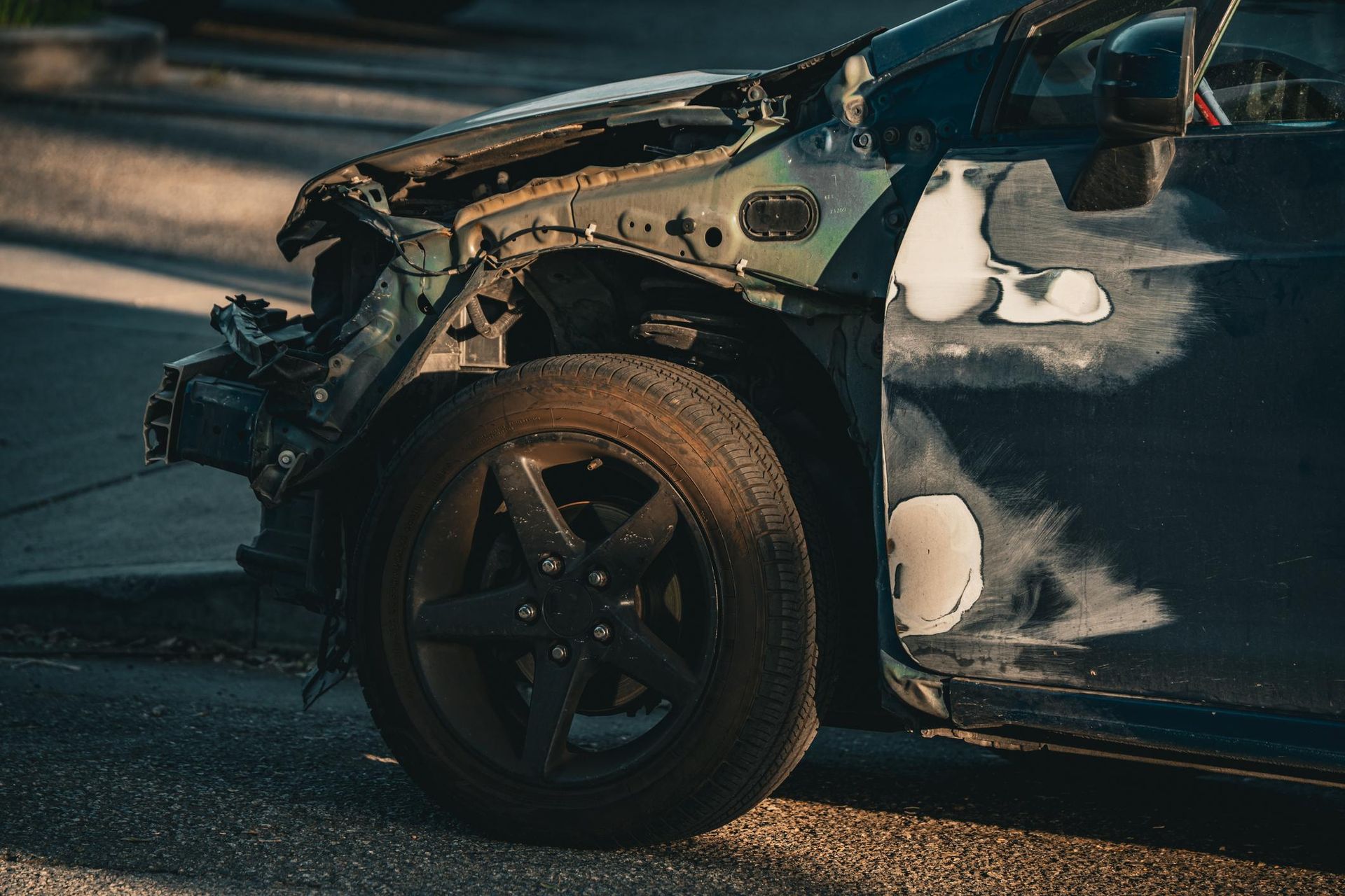 Damaged car, missing front panels, dark tire, parked on a street.