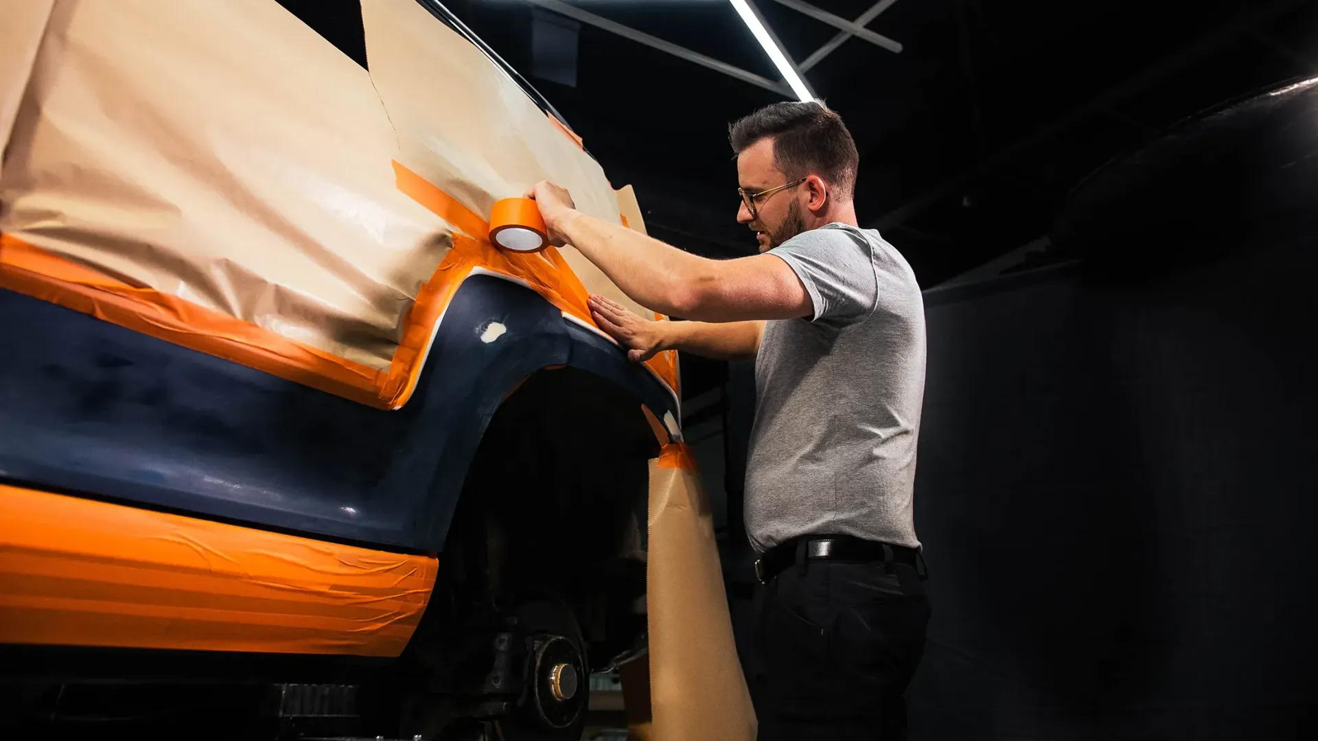 Man taping a vehicle for paint job, indoors with protective paper and paint.