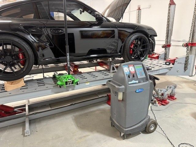 A car is sitting on a lift in a garage next to a machine.