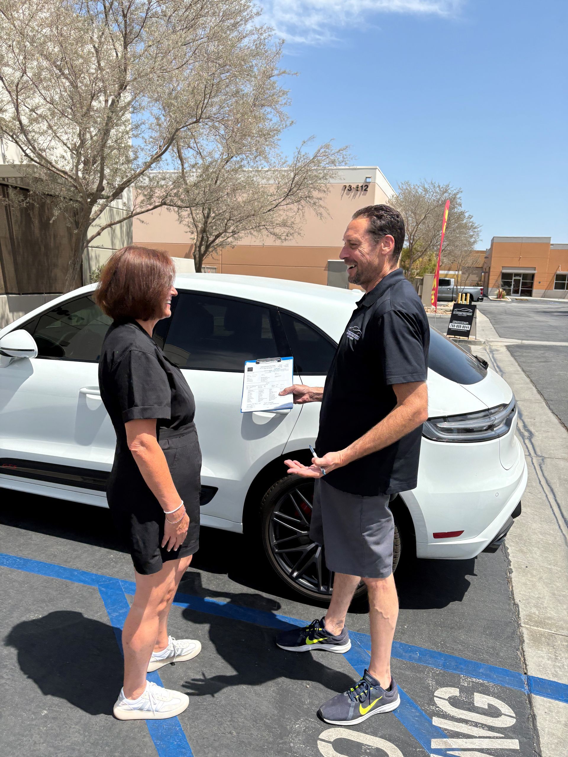 A man and a woman are looking at a clipboard in front of a broken down car.