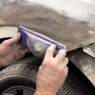 Hands sanding a car body panel with a sanding block.