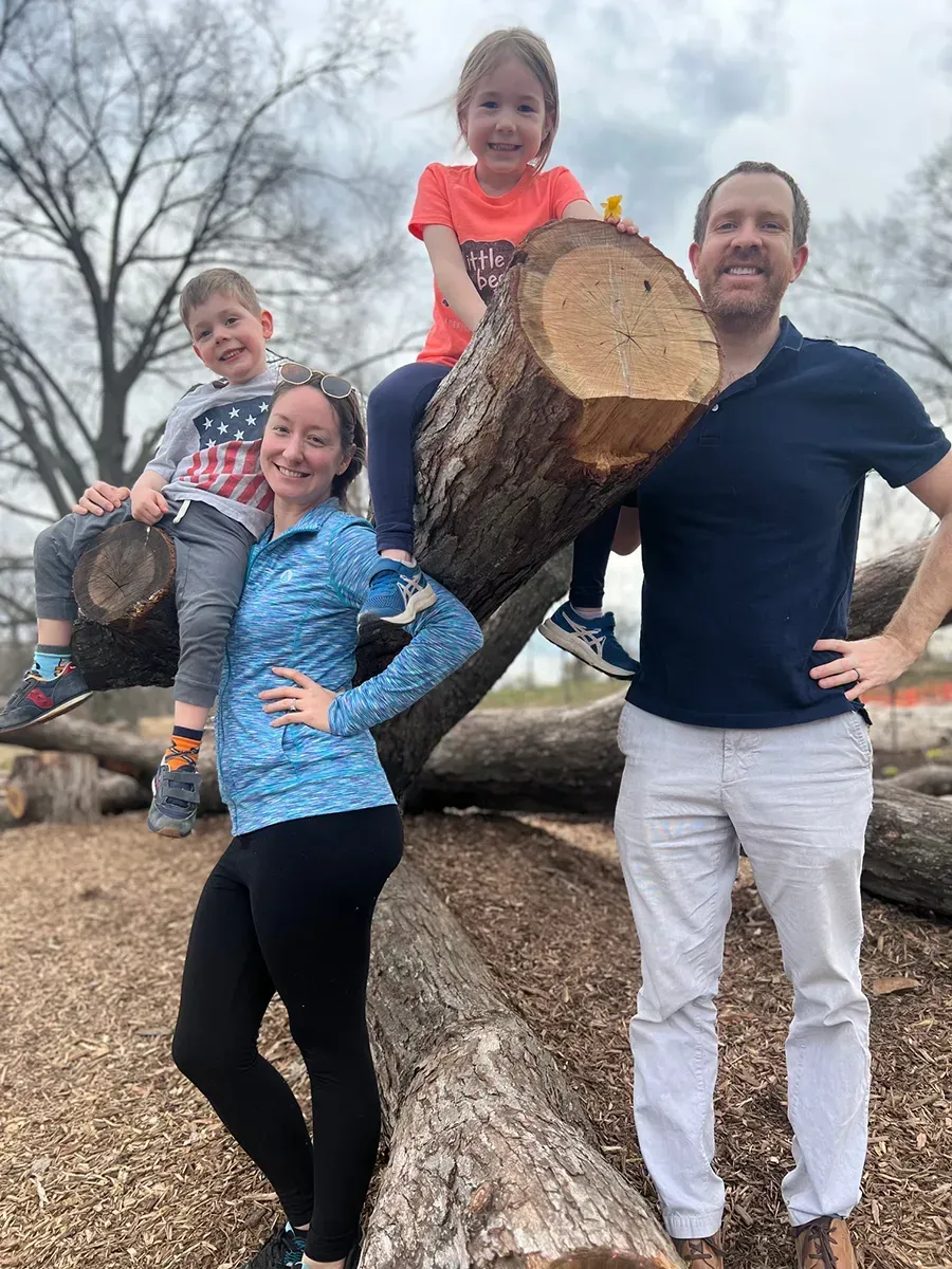 The family of Attorney Andrew Smith is posing for a picture on a log in a park.