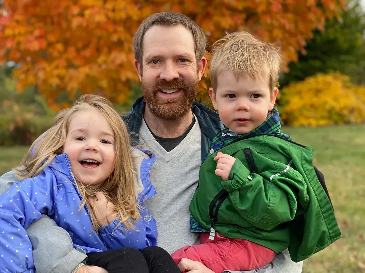 Attorney Andrew Smith is holding two children in his arms in a park.
